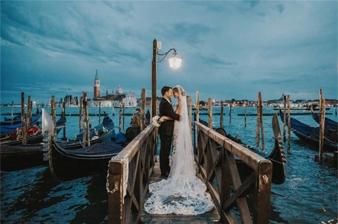 Cô dâu chú rể tạo dáng giữa bốn bề là nước, bức ảnh mang tông màu lạnh. Ảnh được chụp ở Venice, Ý bởi Natalie Watts.