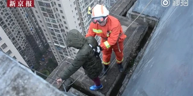 Người lính cứu hỏa tiếp cận và giữ chặt cậu bé đứng ngoài rìa của tòa nhà 33 tầng