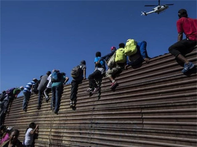  Người di cư leo rào biên giới ngăn Mexico-Mỹ để vào Mỹ. Ảnh: CNN 