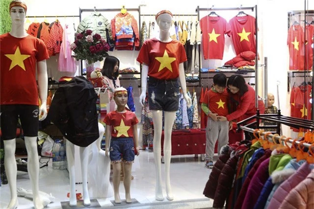  Một bà mẹ đang thử cho con trai chiếc áo in cờ đỏ sao vàng để cổ vũ cho đội tuyển bóng đá Việt Nam. 