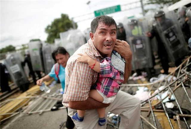  Ông bố Honduras bảo vệ con trong vụ đụng độ giữa đoàn người di cư với lực lượng biên phòng ở Mexico ngày 19/10. 