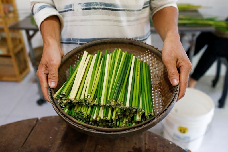 Anh Trần Minh Tiến cầm một chiếc rổ đựng ống hút làm từ cỏ bàng do cửa hàng mình sản xuất. (Ảnh: Reuters)