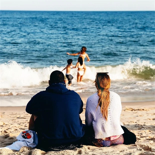Cặp sao ngồi ngắm các con vui đùa với sóng biển.