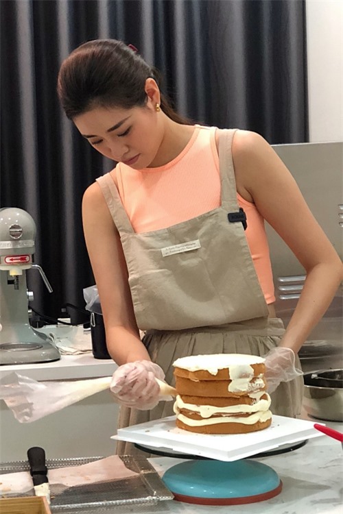 Sau khi lấy bánh ra khỏi lò, cô tiến hành công đoạn phủ kem. Khánh Vân cẩn thận giữ bánh cố định trên khung, xếp thành từng lớp chắc chắn.