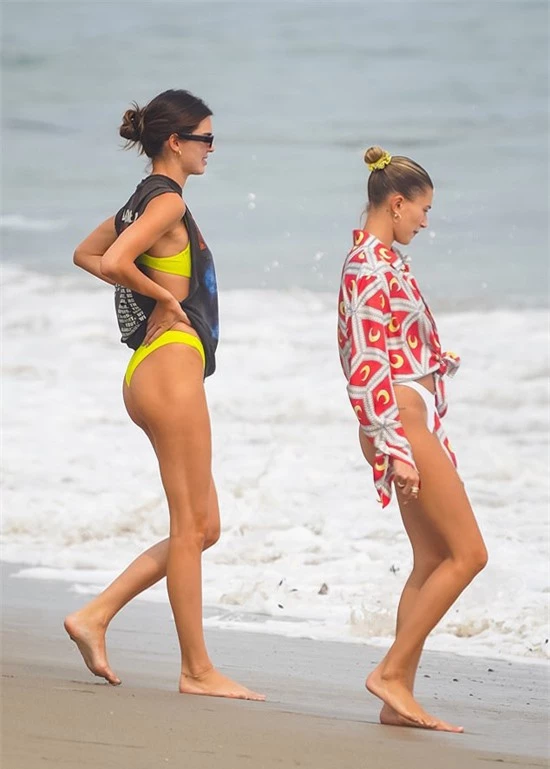 Kendall Jenner mặc bikini vàng trong khi Hailey Bieber diện bikini trắng kết hợp sơmi rực rỡ. Hai người đẹp cùng khoe đôi chân dài săn chắc.