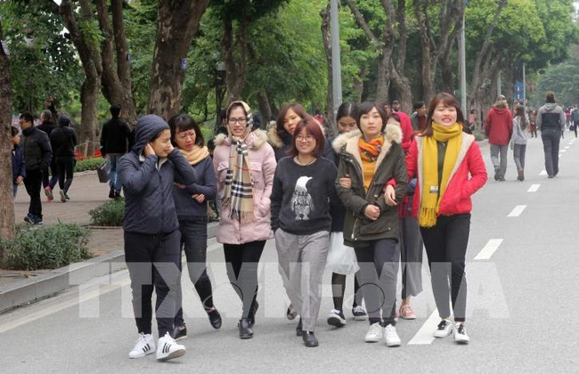 Người dân tại Hà Nội dạo chơi trên phố đi bộ Hồ Hoàn Kiếm đều trang bị cho mình quần áo ấm, quấn khăn, đeo khẩu trang… để chống lại thời tiết lạnh buốt. (Ảnh: TTXVN)