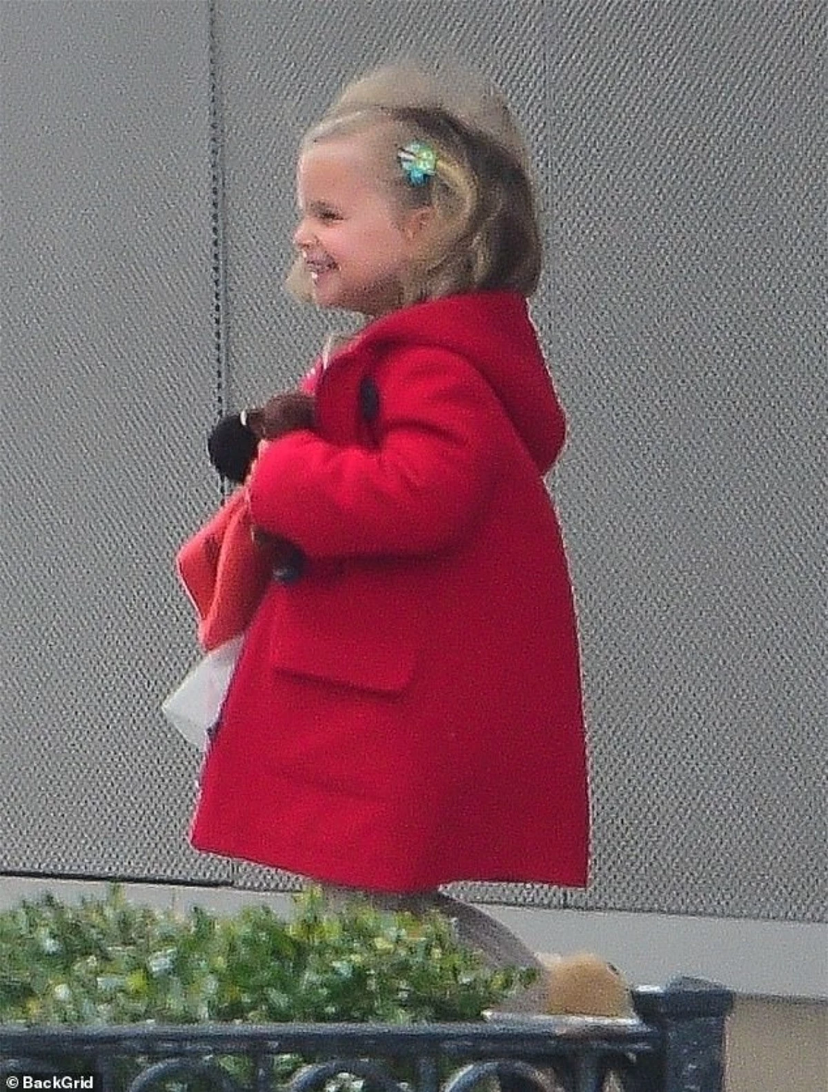 Cô bé xinh xắn với mái tóc cài nơ hoa, áo khoác đỏ vừa vặn.
