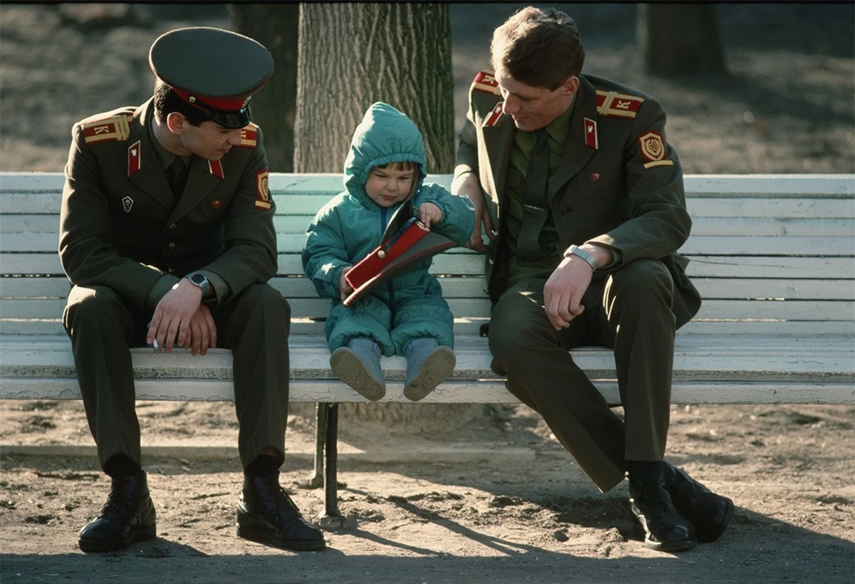 Binh sĩ Liên Xô ngồi trên ghế băng cùng 1 em bé.