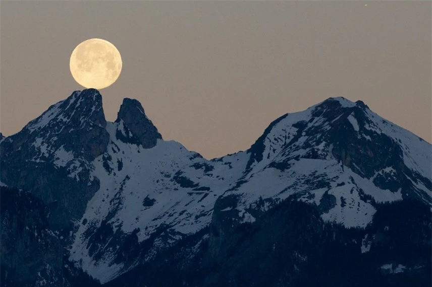 Mặt Trăng từ từ lặn sau ngọn n&uacute;i Les Jumelles ở Chablais Valaisan, nh&igrave;n từ l&agrave;ng Fenalet-sur-Bex ở Thụy Sĩ. Ảnh: Anthony Anex / EPA.