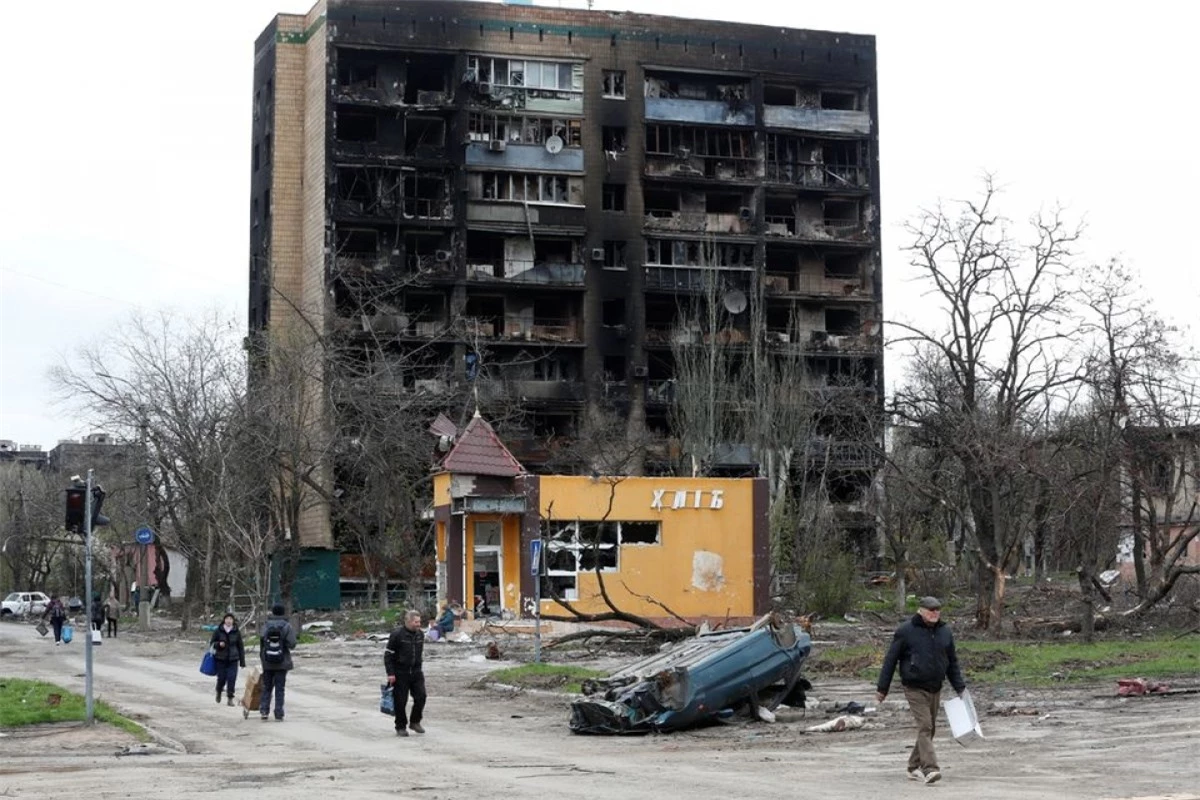 Người dân đi bộ qua một tòa nhà bị phá hủy nghiêm trọng trong cuộc chiến giữa Nga và Ukraine ở phía nam thành phố cảng Mariupol, Ukraine ngày 21/4/2022. Ảnh: Reuters