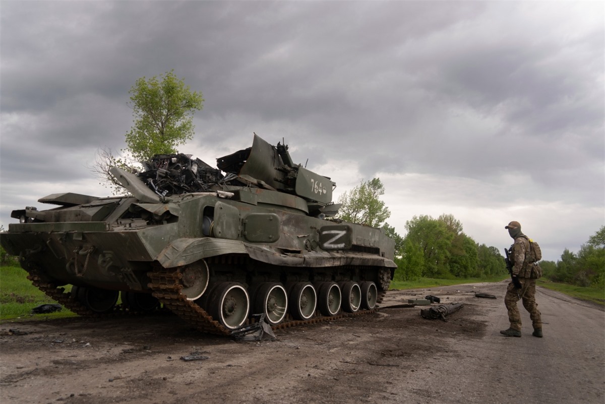 Một quân nhân Ukraine đi ngang qua một chiếc xe tăng bị hư hỏng gần Kutuzivka, phía bắc Kharkiv, đông Ukraine hôm Chủ nhật. (Ảnh: AP)