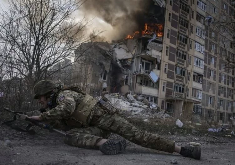 Một binh sĩ Ukraine ẩn nấp trước tòa nhà bốc cháy và đổ nát ở Avdiivka. Ảnh: AP.