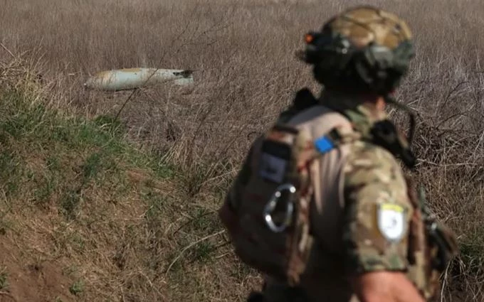 Một binh sĩ đi ngang qua một quả bom FAB-500 chưa nổ của Nga trên cánh đồng gần làng Ocheretyne, cách Avdiivka không xa. Ảnh: AFP
