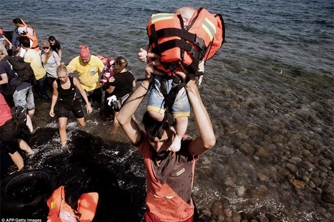 Một người đàn ông Syria bế bé trai đeo áo phao khi nhóm người của họ vừa đến đảo Lesbos.